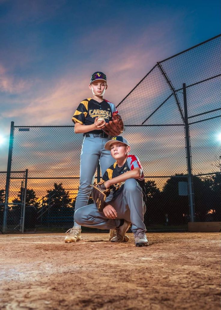 two baseball players posing for a photo in front of a fence at night with the sun setting behind them