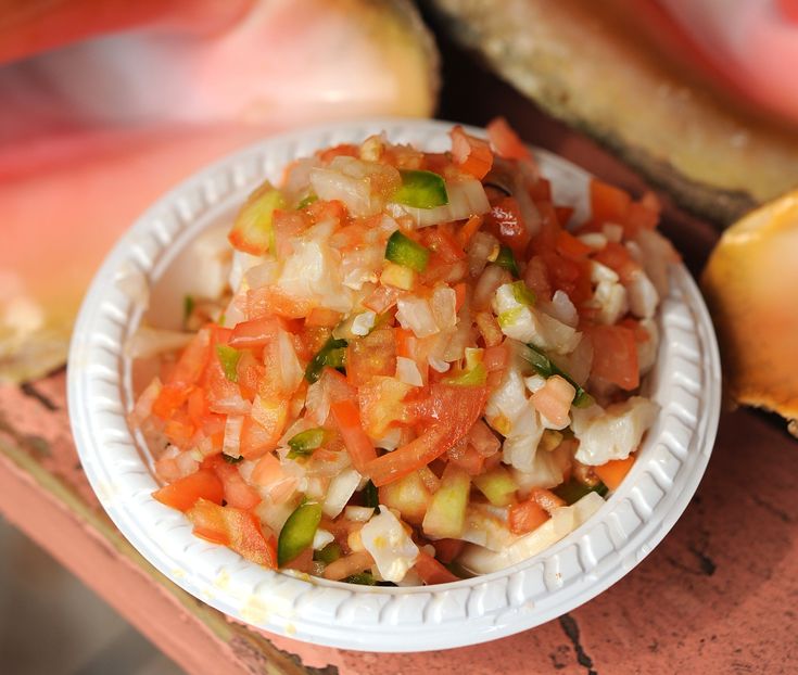 a paper plate filled with chopped vegetables on top of a table next to sliced bread