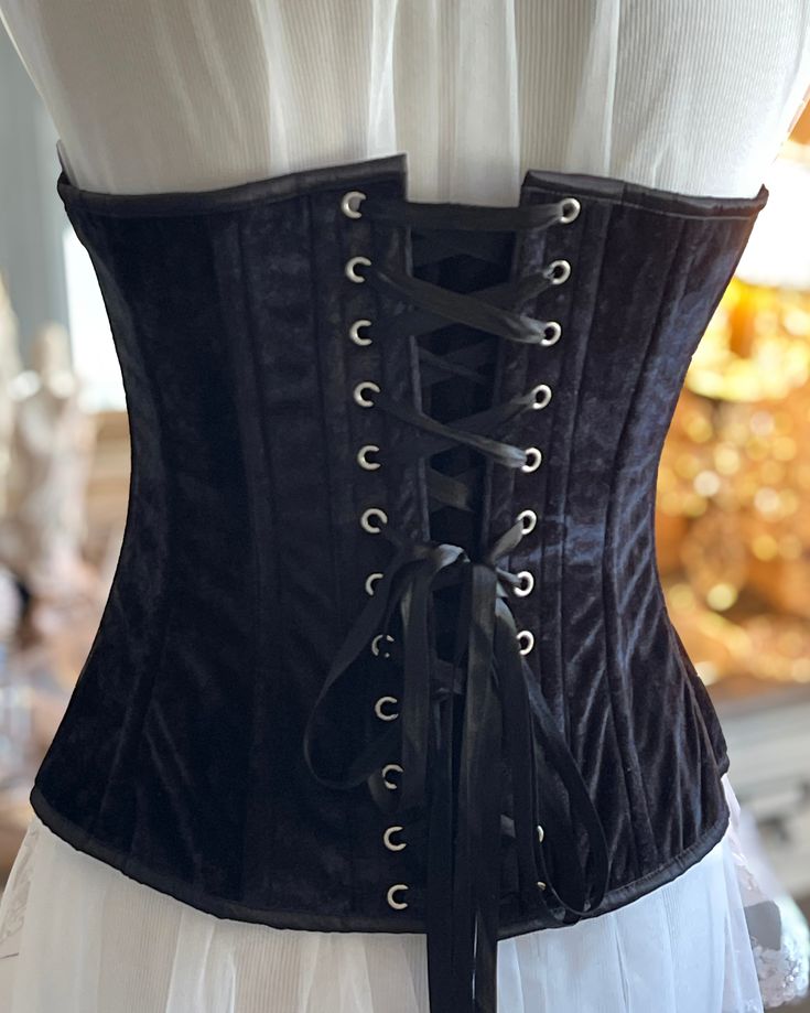 Transform your look with the Bious Corset. Made with luxurious black velvet, this overbust corset will enhance your curves and give you a confident, alluring silhouette. Elevate your style and make heads turn with this must-have fashion staple. The Bious Corset Gorgeous Black Velvet Over Bust Corset. Velvet lined with cotton and steel boned. Front metal busk Opening and back lacing with white satin ribbon. The center front length is 14.5" and back length 13".New colors added Black satin.Sizes X- Elegant Boned Corset For Costume, Elegant Costume Corset With Boning, Elegant Boning Corset For Costume, Elegant Black Underbust Corset Dress, Black Corset With Corset Back For Costume, Elegant Underbust Corset For Costume Party, Black Costume Corset With Corset Back, Elegant Black Corset Dress With Boning, Elegant Black Boned Corset Dress