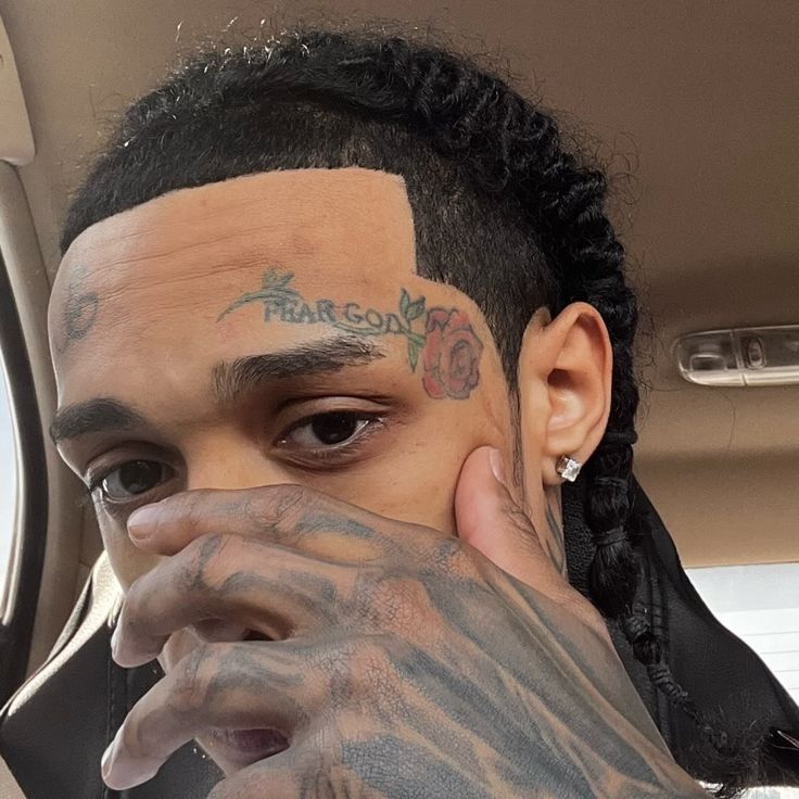 a man with tattoos on his face and hand covering his face while sitting in a car