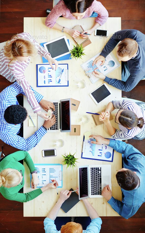 four people sitting at a table with laptops and notebooks in front of them