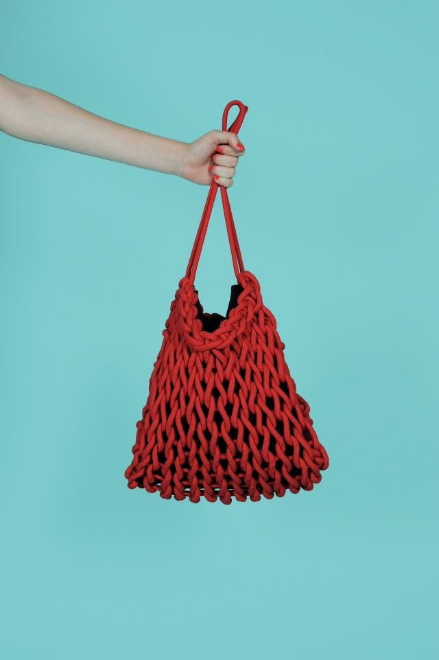 a woman's hand holding a red knitted bag on a blue background,