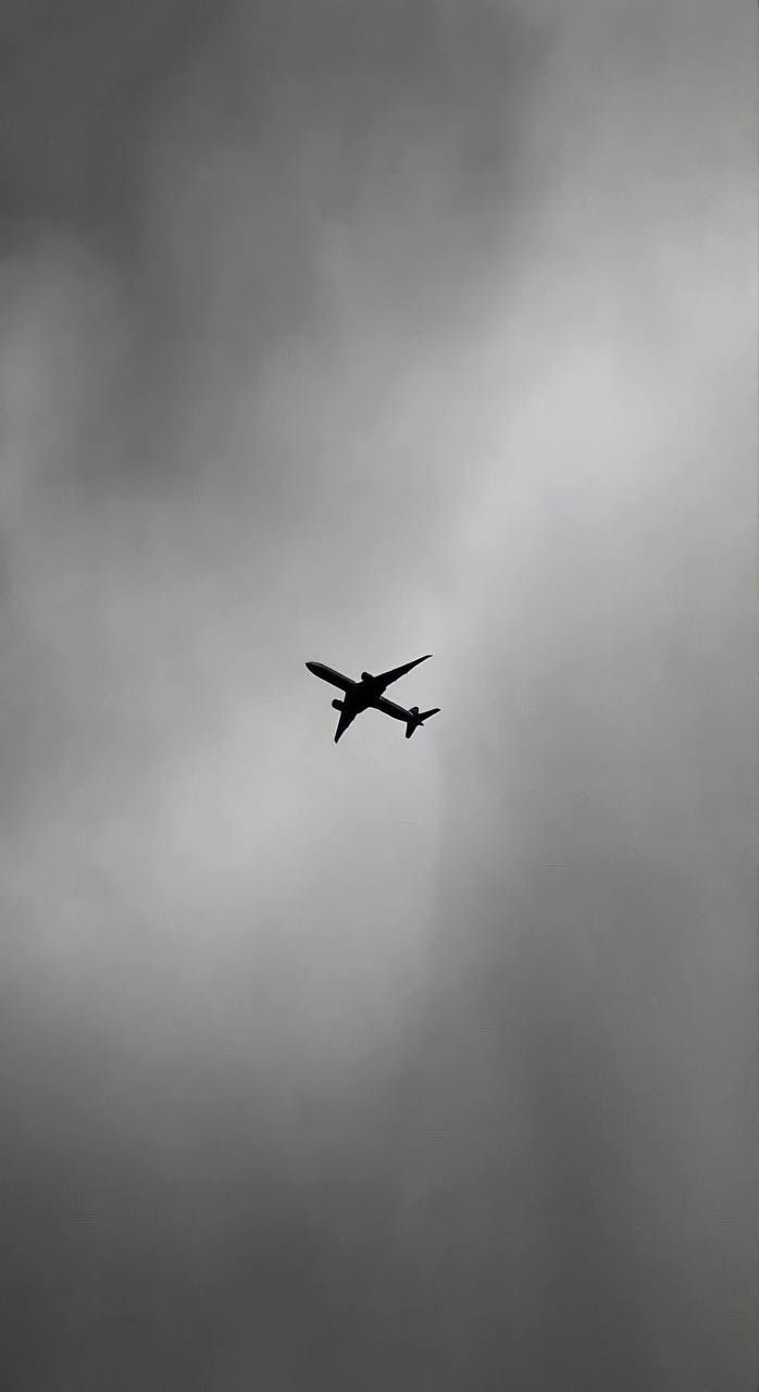 an airplane is flying in the sky on a cloudy day with dark clouds behind it