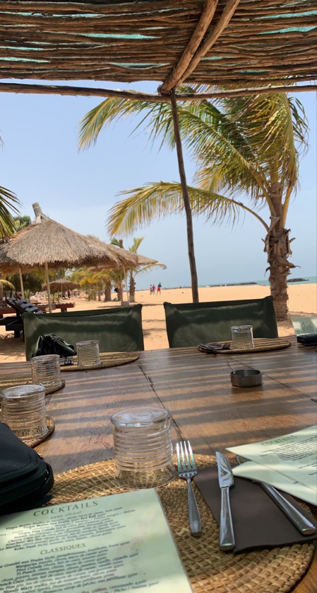 the table is set with place settings for two people on the beach, and there are palm trees in the background