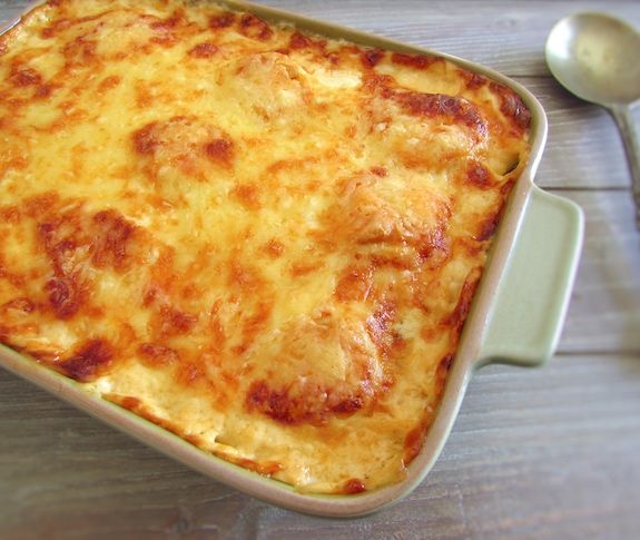 a casserole dish with cheese on top and spoon next to it, sitting on a wooden table