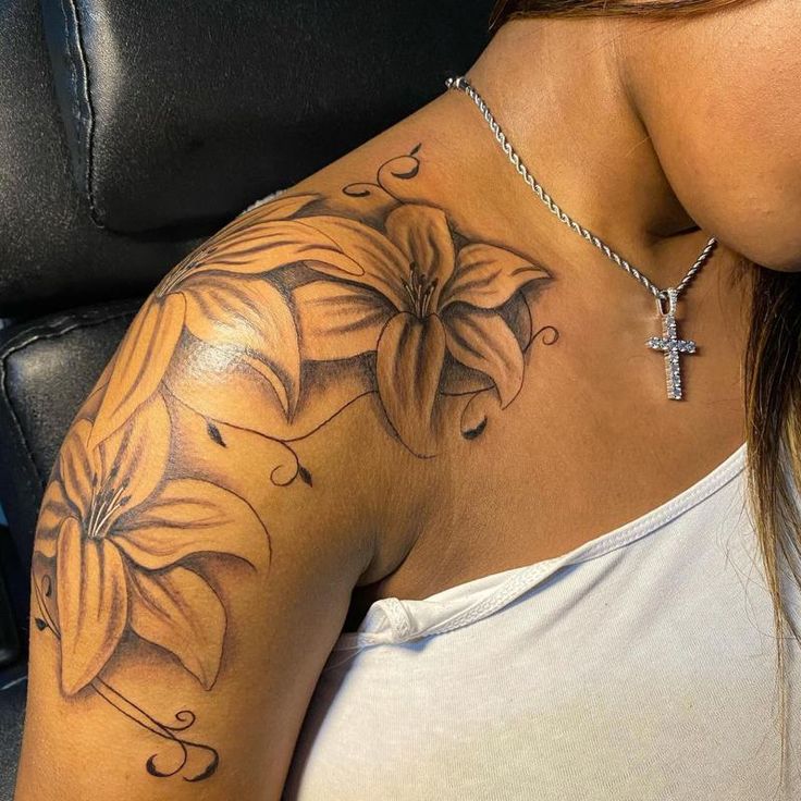 a woman with a cross and flowers on her back shoulder tattooing it's upper half