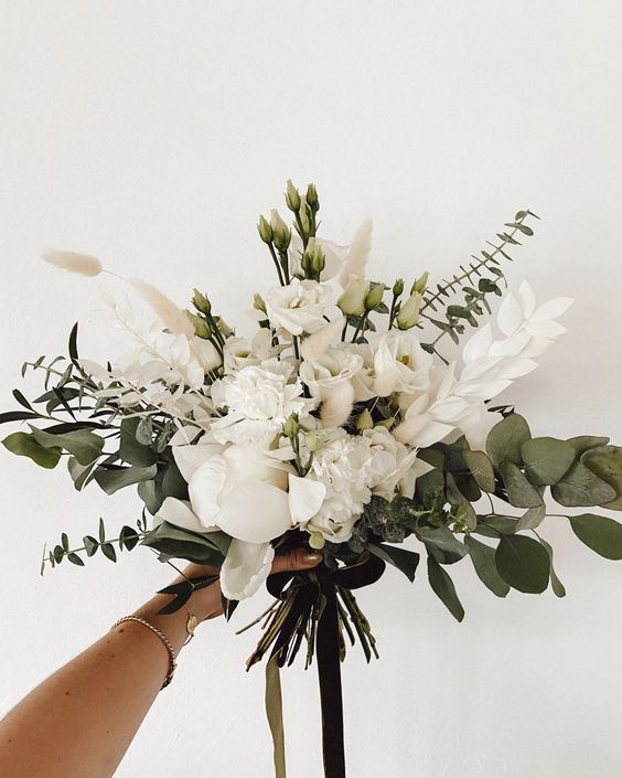 a bouquet of white flowers and greenery being held by someone's hand