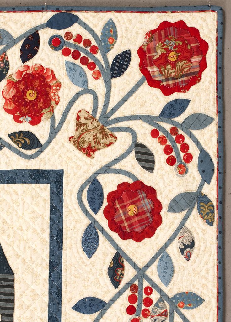 a quilted wall hanging with red and blue flowers on it's border,