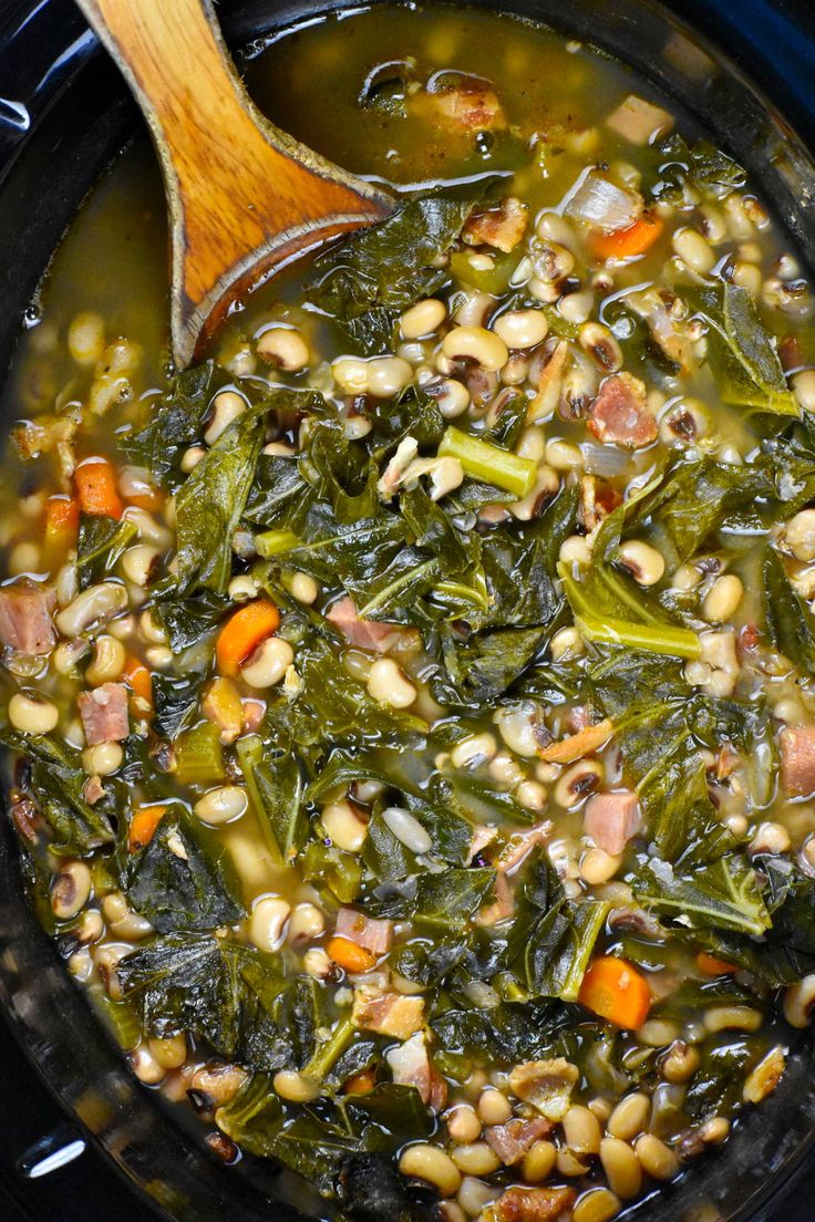 a pot filled with beans and greens next to a wooden spoon