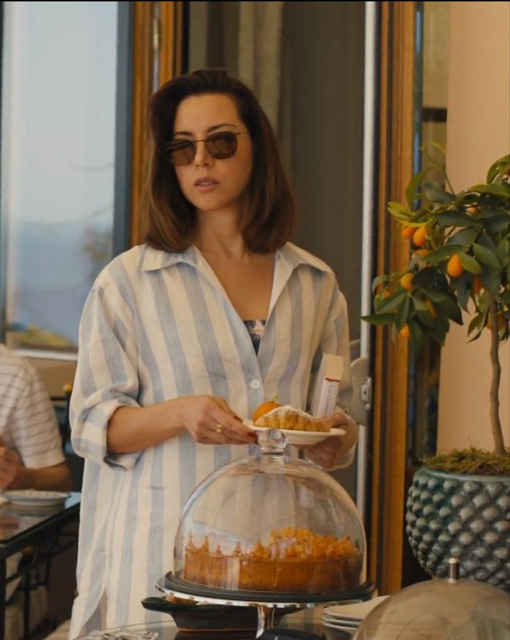 a woman is serving food from a glass dome on a table with other people in the background