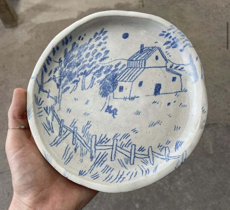 a hand holding a blue and white bowl with a house on the side in it