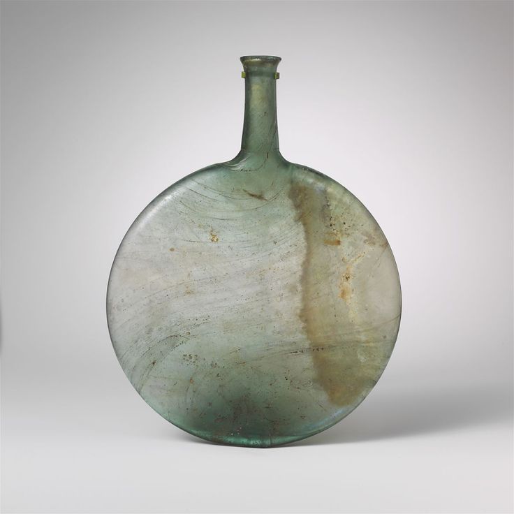 an old green glass bottle sitting on top of a white table next to a gray wall