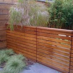 a wooden fence in front of a building with grass growing on the ground and bushes next to it