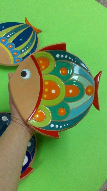 a hand is holding two colorful fish shaped plates on a green surface with blue, yellow and orange designs