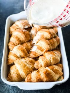 someone pouring milk into a baking dish filled with croissants