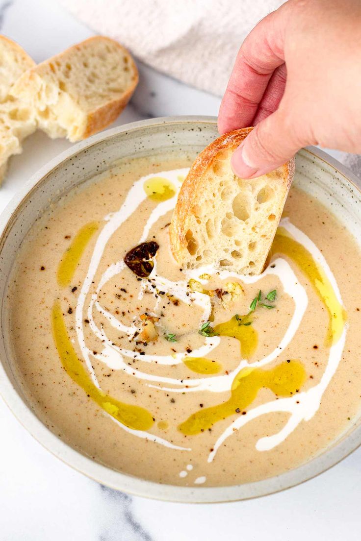 a person dipping bread into a bowl of soup