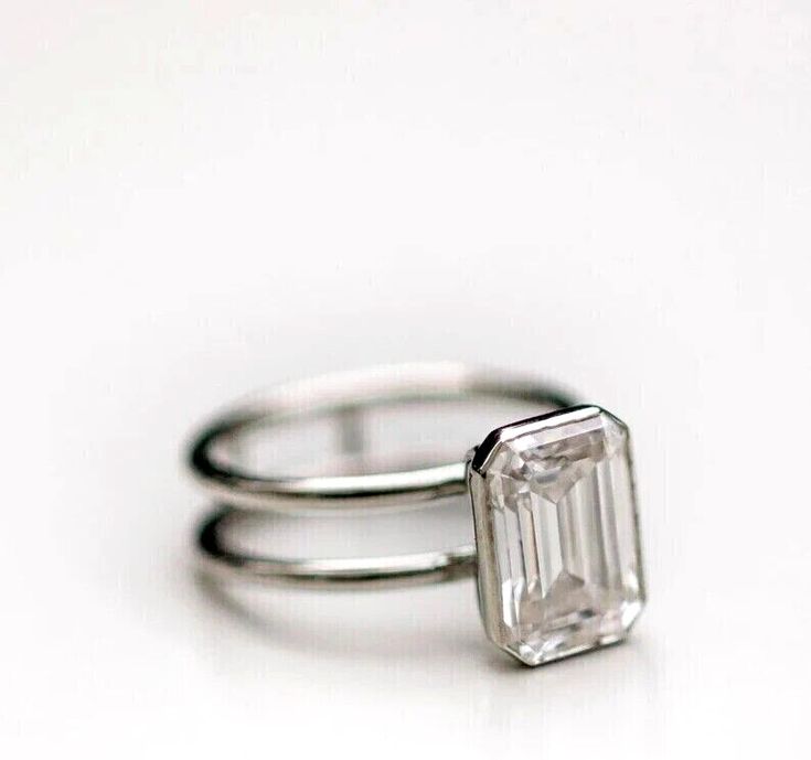 two wedding rings with an emerald cut diamond on each one, set against a white background