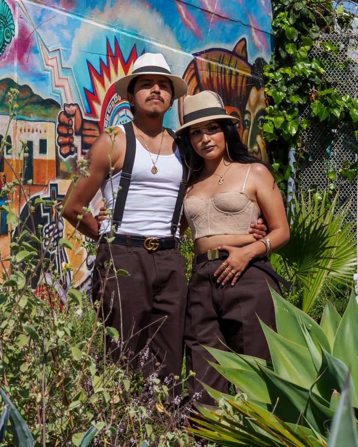 two people standing next to each other in front of a mural