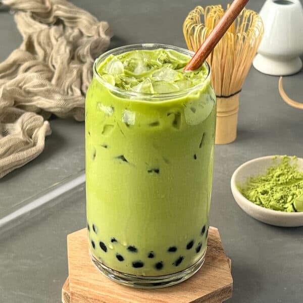 a green smoothie in a glass on a wooden stand with other ingredients around it