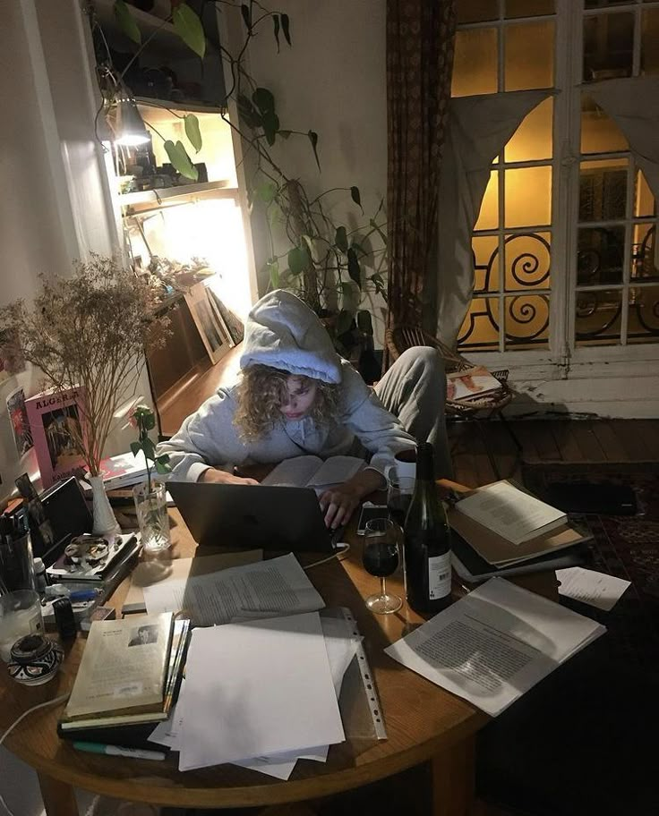 a person sitting at a table with books and papers on it while using a laptop