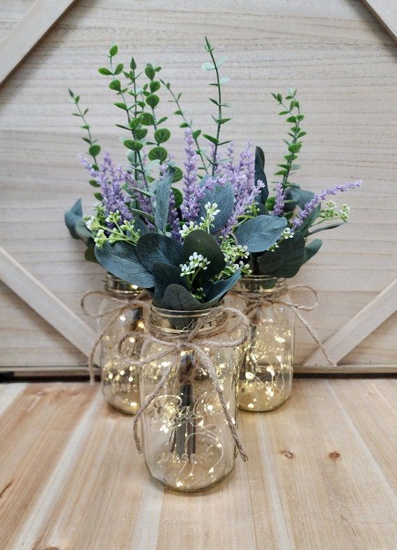 three mason jars filled with flowers and greenery