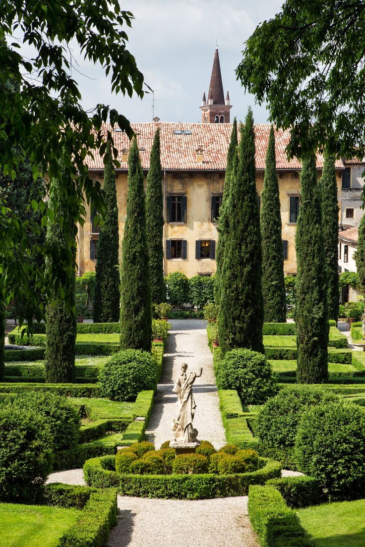 an outdoor garden with hedges, trees and a statue in the center surrounded by greenery