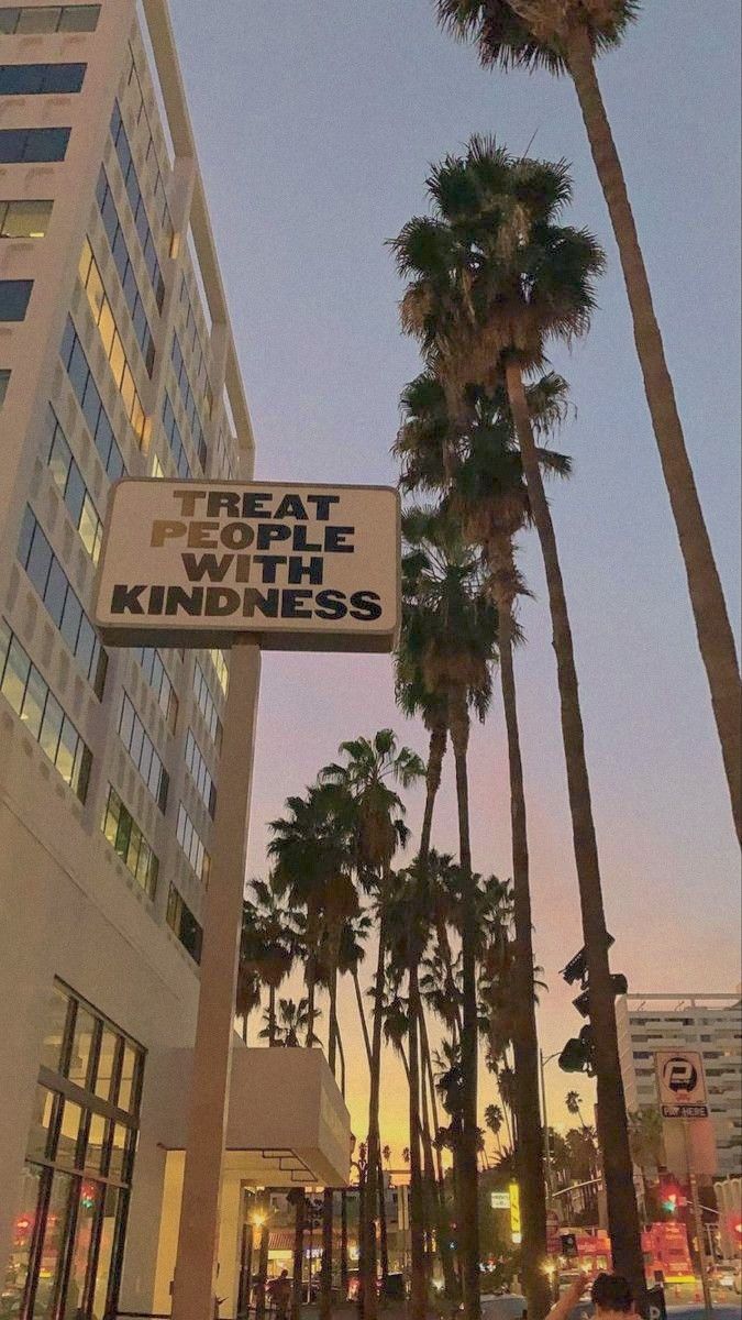 palm trees line the street in front of a building with a sign that reads that place with kindness