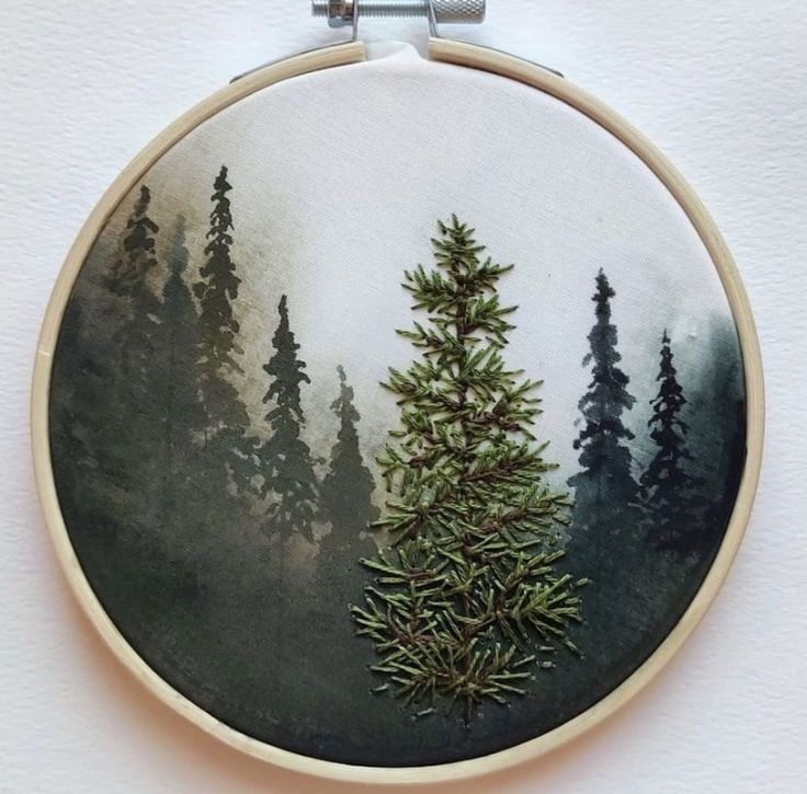 an embroidery project with pine trees in the forest on it's hoop hanging from a wall