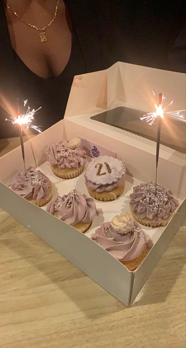 a box filled with cupcakes covered in frosting and sparklers next to a woman