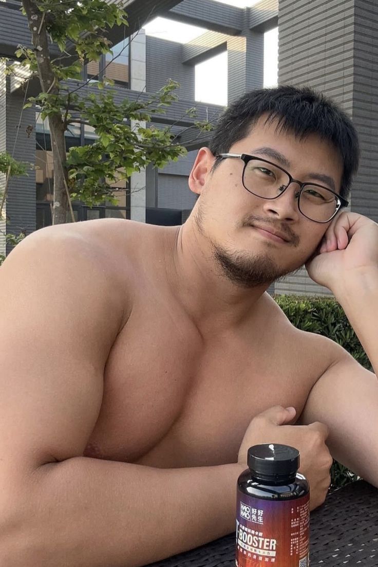 a shirtless man with glasses sitting on a bench next to a bottle of water