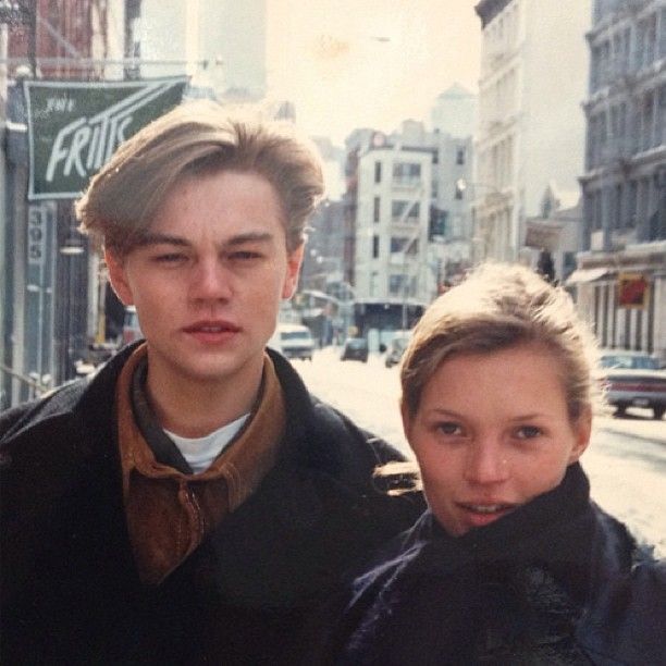 two young men standing next to each other on a city street with buildings in the background