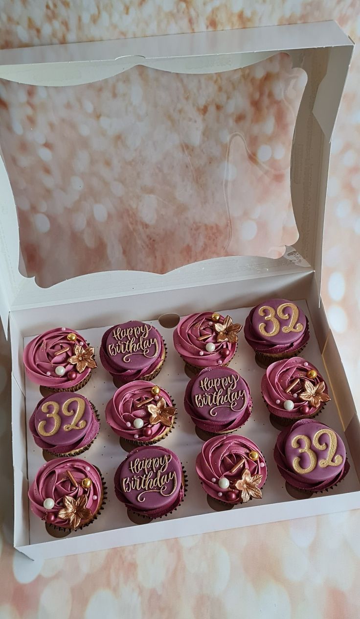 twelve cupcakes with pink frosting and gold decorations in a white cardboard box