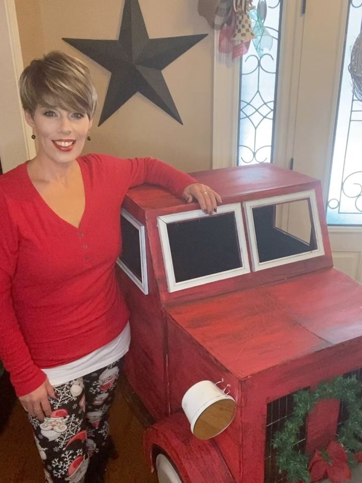 a woman standing next to a red wooden toy truck with windows on it's side