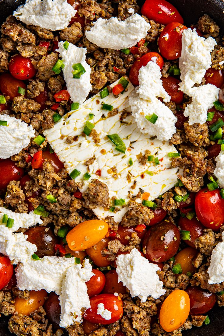 a skillet filled with meat, vegetables and feta cheese on top of it