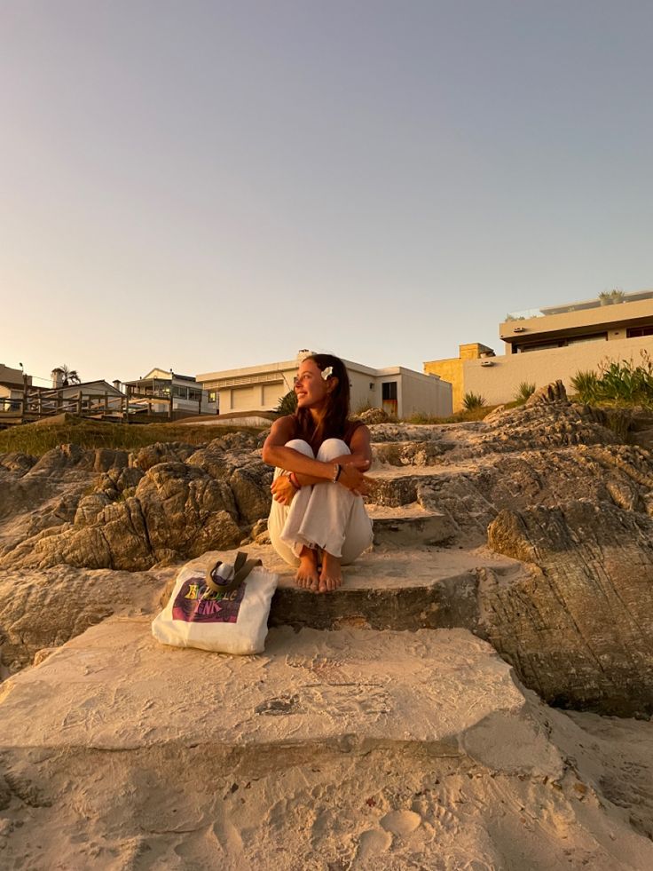 a woman sitting on some rocks near the ocean