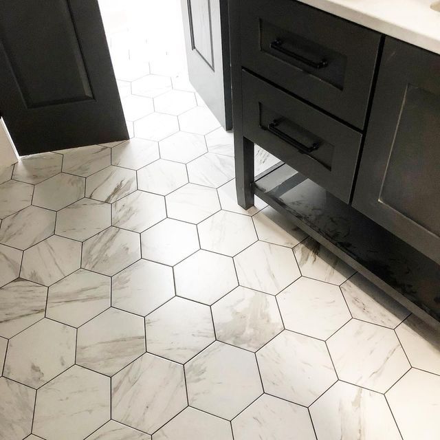 a bathroom with black cabinets and white hexagonal tiles on the floor, along with a marble counter top