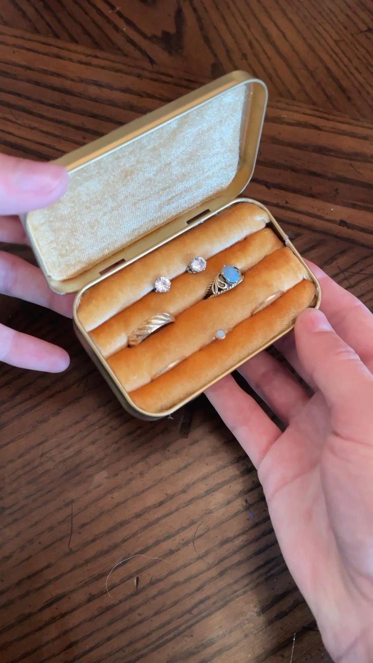 a person holding an open box with rings in it on top of a wooden table