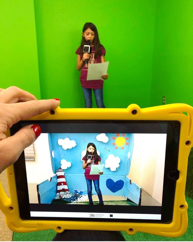 a person holding up a yellow tablet in front of a green room with a girl