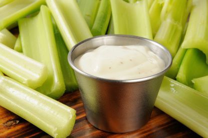 celery sticks and dip in a small metal cup on a wooden cutting board