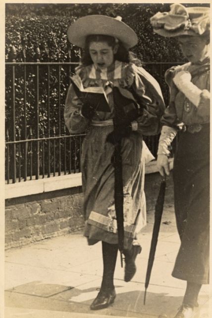 an old black and white photo of two women with hats on walking down the street