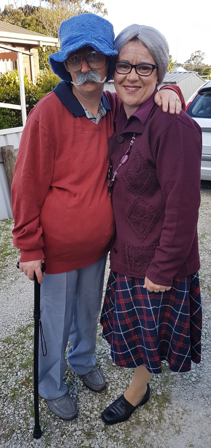 an older couple is posing for the camera in front of their house, wearing hats and holding canes