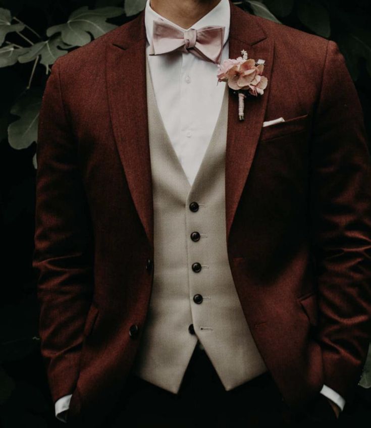 a man in a suit and bow tie standing next to some plants with his hands in his pockets