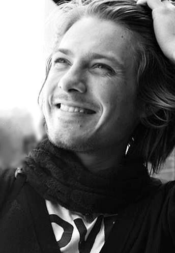 a black and white photo of a man with his hair in a bun smiling at the camera