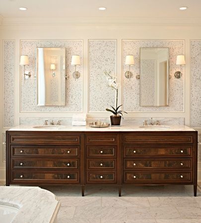 a bathroom with double sinks and two mirrors on the wall next to each other in front of a bed