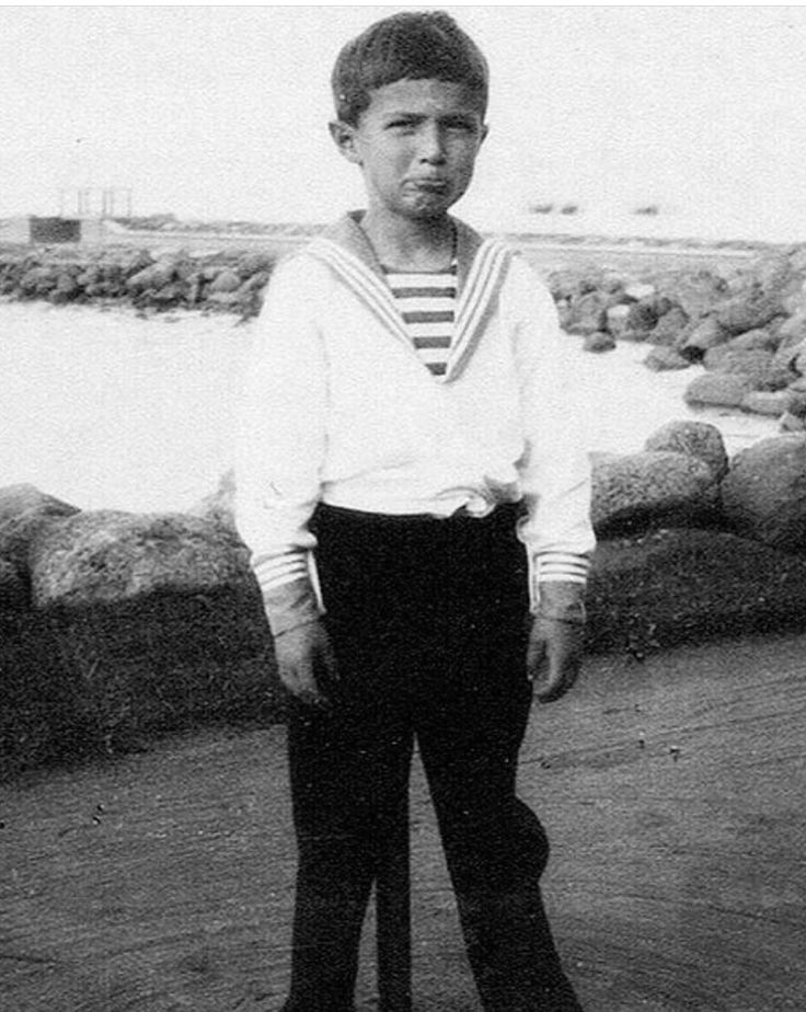 an old black and white photo of a young man in sailor's outfit standing on the beach