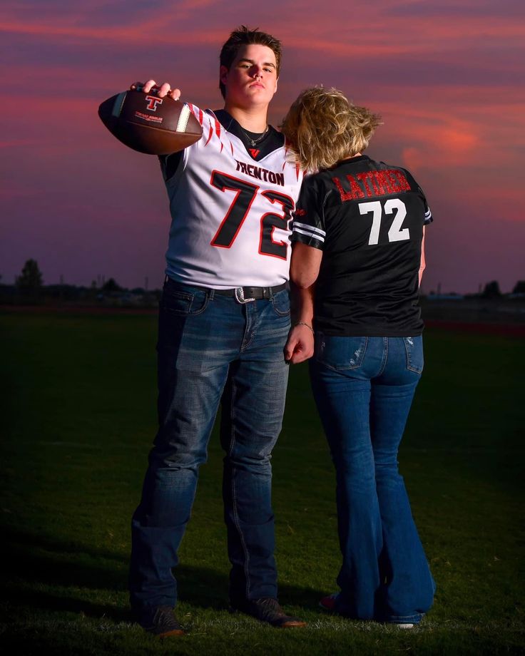 a man and woman standing next to each other on a field holding a football ball