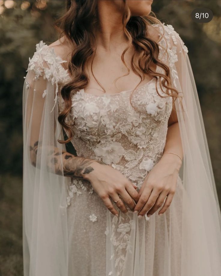 a woman with long hair wearing a wedding dress and veil in front of some trees