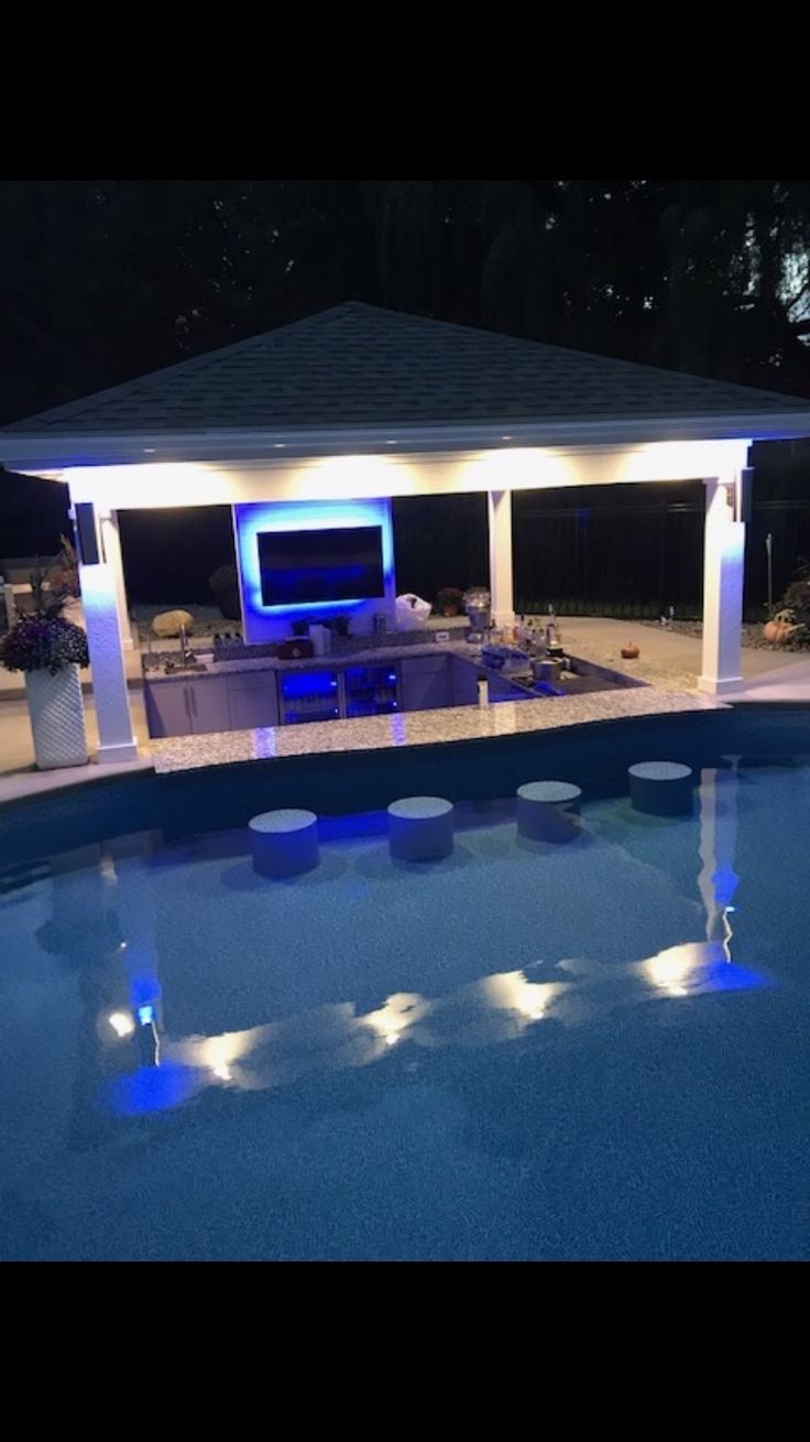 a pool with lights around it and a tv on the wall next to an outdoor living area