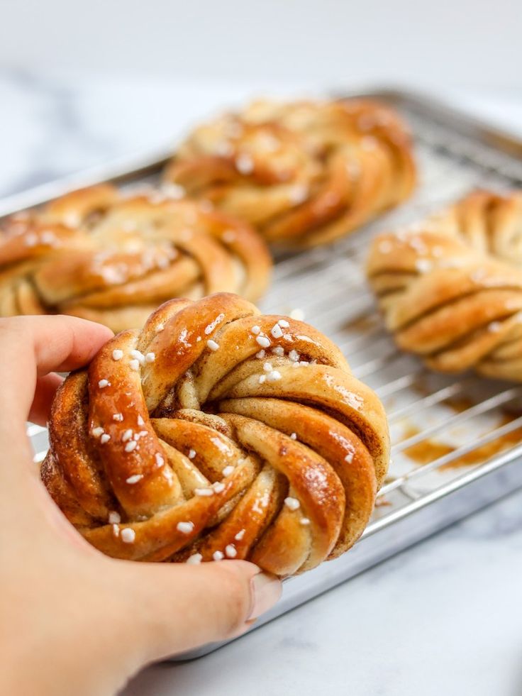 a person holding a pastry in front of some other pastries on a baking sheet