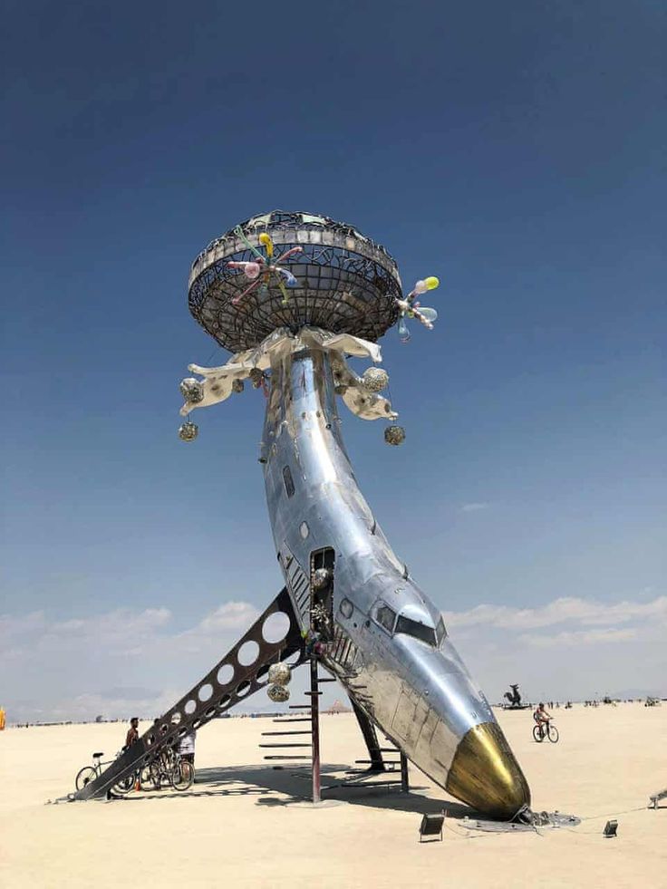 an airplane sculpture on the beach with people walking around